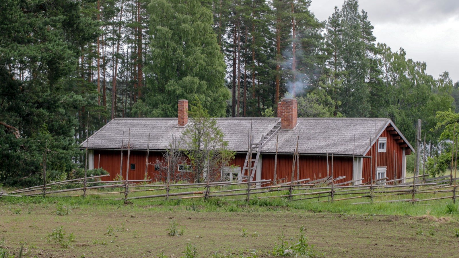 Punainen hirsirakennus ja aita Korteniemen perinnetilan pihapiirissä
