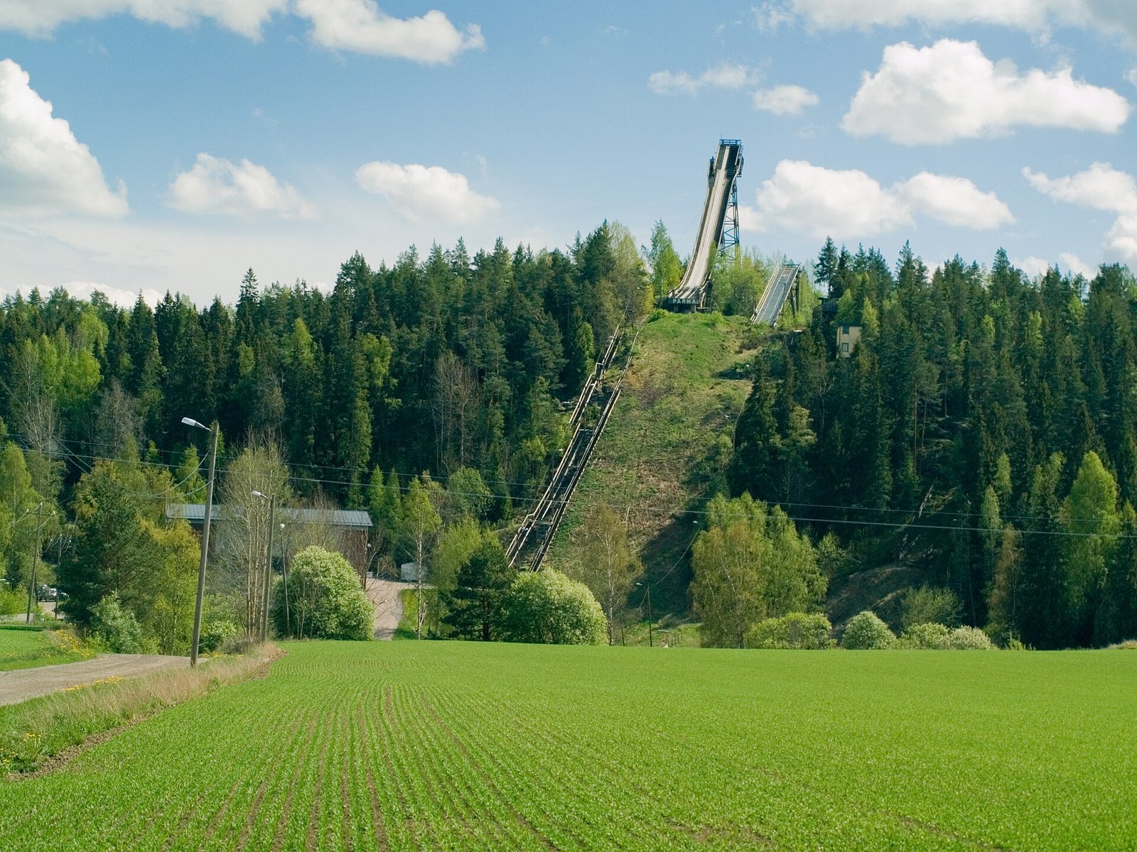 Mäkihyppymäki metsäisellä rinteellä ja pelto etualalla