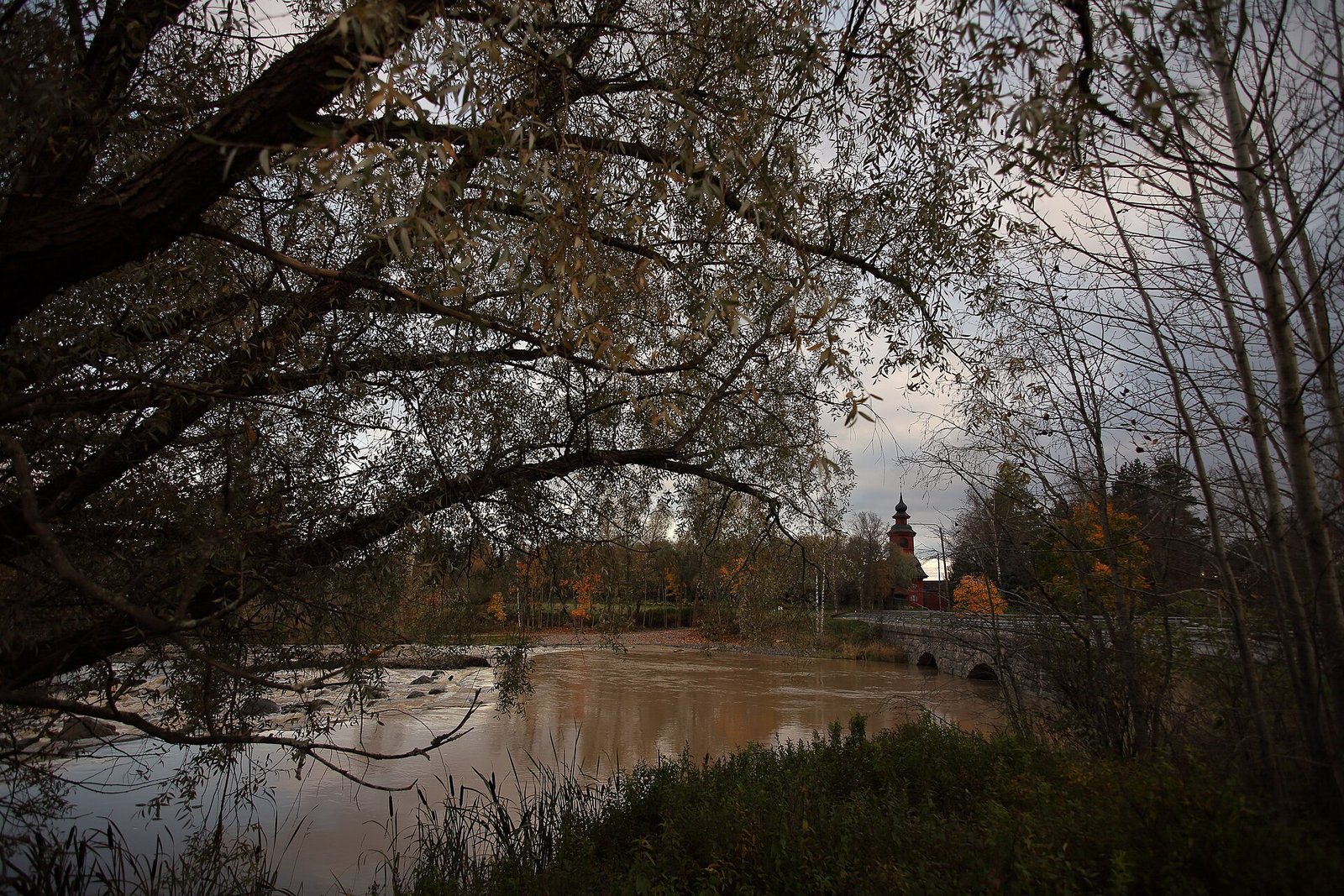 Kivinen holvisilta ja kellotapuli Paimionjoen yllä syksyllä