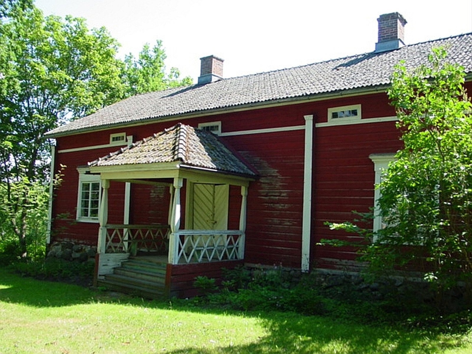 Punainen puinen pappilarakennus puutarhan keskellä
