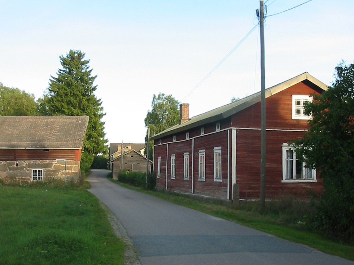 Kapea kylätie, punainen pitkä puurakennus ja kivinen aitta